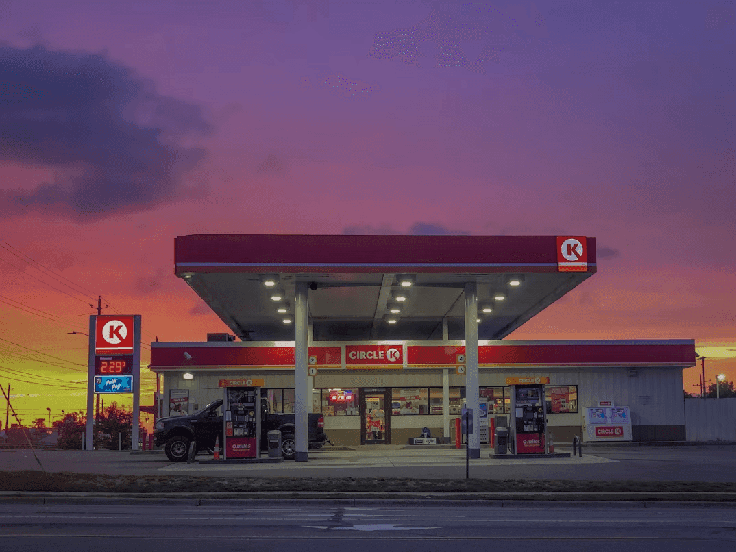 The brightly lit storefront of a Circle K gas station under a colorful sunset sky