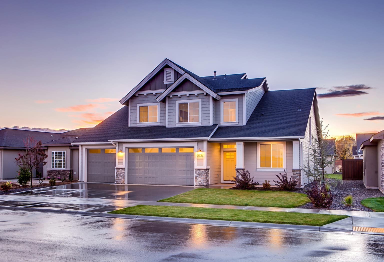 Modern suburban house with a two-car garage at dusk, with lights on inside